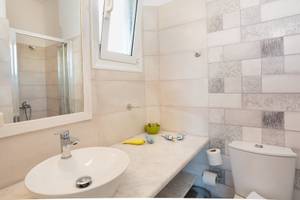 Badezimmer im Pyrgaki Hotel mit weißem Waschbecken, Spiegel, Duschkabine und gefliester Wand.