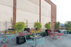 Dachterrasse des Leonardo Royal Hotel Amsterdam mit farbenfrohen Tischen und Stühlen.