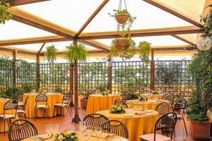 Garten-Terrasse des Pineta Palace Hotels mit runden Tischen, Stühlen und gelben Tischdecken, umgeben von Pflanzen und Blumen.