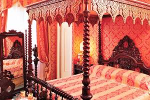 Ein rotes Schlafzimmer im Metropole Hotel mit einem Baldachinbett und goldenen Wandverzierungen.