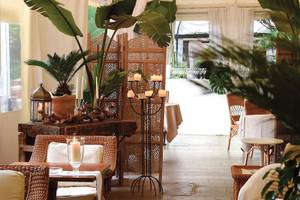 Innenbereich des Metropole Hotels mit braunen Korbstühlen, einem Tisch mit Kerzen und Pflanzen.