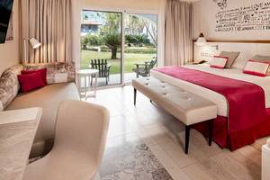 Hotelzimmer im Catalonia Bayahibe mit Blick auf den Garten, großem Bett, Sitzbereich und offenem Balkon.