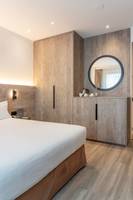 Ein modernes Hotelzimmer mit einem Bett, Holzboden und einer Wand mit Spiegel und Einbauschränken.