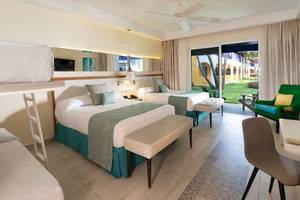 Hotelzimmer im Catalonia Bayahibe mit drei Betten, Schreibtisch und Balkonzugang.