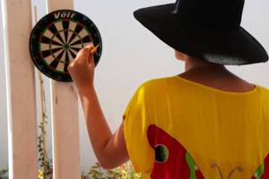 Eine Person in einem gelben T-Shirt wirft einen Dart auf ein Zielbrett.