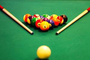 Ein Pooltisch mit bunten Kugeln und Stöcken, die Kugel Nummer 1 ist hervorgehoben.