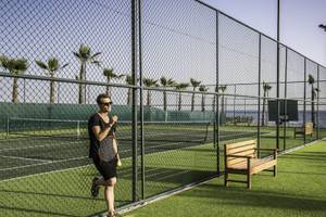 Ein Mann mit Tennisschläger und Ball steht an einem Tennisplatz im Rubi Platinum Spa Resort.