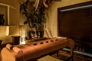 Massageraum im Delphin Deluxe Hotel mit Hocker, Pflanzen und Holzmöbeln.