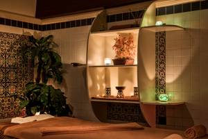 Spa-Behandlungsraum im Delphin Deluxe Hotel mit einem Massagetisch, Pflanzen und dekorativen Elementen.