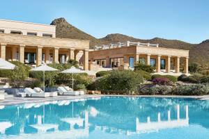 Außenpool mit Lounge-Liegestühlen und weißen Sonnenschirmen vor dem Cape Sounio Grecotel Resort.