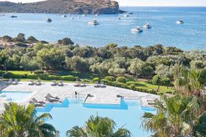 Aussicht auf den Poolbereich des Cape Sounio Grecotel Resorts mit vielen Liegestühlen und Booten im Meer