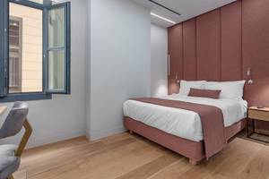 Hellenic Vibes Smart Hotel Athen, Schlafzimmer mit Doppelbett, rotem Kopfteil und Holzboden.