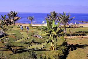 Golfplatz am Strand des Constantinou Bros Athena Beach Hotels mit zwei Spielern und Palmen.