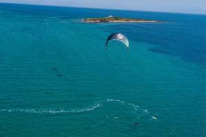 Ein Segelparaglider fliegt über dem blauen Meer mit einer kleinen Insel im Hintergrund.