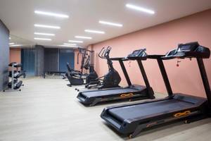 Fitnessraum im Hotel Dolce Athens Attica Riviera mit mehreren schwarzen Laufbändern und Trainingsgeräten.