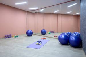 Fitnessraum im Hotel Dolce Athens Attica Riviera mit Spiegelwänden, blauen Gymnastikbällen und Trainingsgeräten.