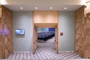 Eingangsbereich des Konferenzraums im Hotel Dolce Athens Attica Riviera mit geometrischen Holzwandverkleidungen und einer Fernsehwand