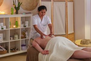 Eine Frau im weißen Dienstmädchenkostüm führt eine Massagebehandlung in einem Zimmer im Aparthotel Marins Playa durch.