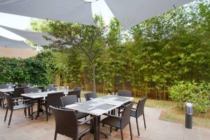 Foto von der Terrasse des Bakour Garbi Cala Millor Hotels mit Tischen und Stühle, umgeben von Bambusbepflanzung.