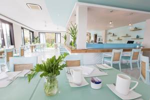 Innenansicht des Restaurants im TIA Wellness Resort mit blauen Tischen, Stühlen und einer Theke.