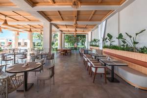 Innenansicht des Restaurants im Sherwood Exclusive Kemer Hotel mit Tischen, Stühlen und Pflanzen.
