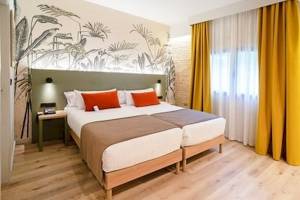 Schlafzimmer im DWO Valencia mit zwei Betten, grüner Kopfteilwand, Pflanzentapete und gelben Vorhängen.