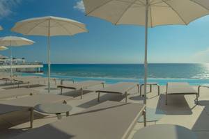 Terrasse des RH Bayren & Spa Hotels mit weißen Sonnenliegen und Sonnenschirmen am Meer