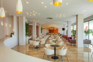 Innenbereich des RH Bayren & Spa Hotels mit vielen Tischen und Stühlen, Pflanzen und hängenden Lampen.