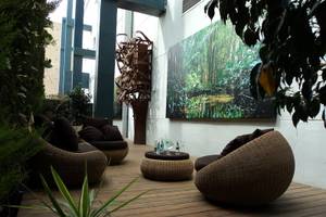 Gartenlounge im Principal Afilliated by RH mit Korbsesseln und einem großen Gemälde an der Wand.