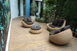 Terrasse mit Korbmöbeln und einem Tisch im Freien, umgeben von Pflanzen und einer Wandmalerei.