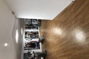 Fitnessstudio mit Holzboden und Fitnessgeräten, darunter ein Laufband und ein Rudergerät.
