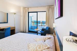 Hotelzimmer mit Meerblick, Bett, Schreibtisch und zwei Stühlen.