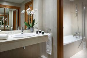 Badezimmer im Hotel Exe Rey Don Jaime mit Waschbecken, Spiegel, Badewanne und Orchideen.
