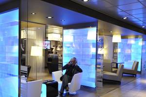 Mann mit Kopfhörern in einer Hotel-Lounge, mit blauen Lichtern und weißen Möbeln im Hintergrund.