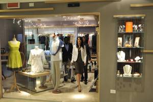 Eine Boutique mit Kunden, die Kleidung und Schmuck betrachten, und Vitrinen, die Accessoires und Uhren präsentieren.