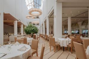 Innenansicht des Restaurants im Lindos Royal Resort mit runden Kronleuchtern und eleganten Esstischen.