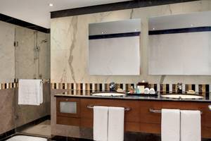 Ein Badezimmer im Al Ain Rotana Hotel mit einer Dusche, zwei Waschbecken und Spiegeln.