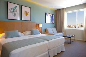 Doppelzimmer im Riu Plaza Espana mit zwei Betten, Sofa, Tisch und Fenster mit Stadtblick.