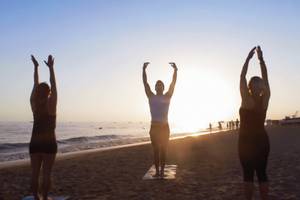 Drei Frauen praktizieren Yoga auf dem Strand vor dem TUI BLUE Side Hotel.