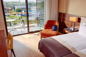 Doppelzimmer im TUI BLUE Side Hotel mit Balkon, zwei Betten, Tisch, Stuhl und Aussicht auf Pool und Rutsche.