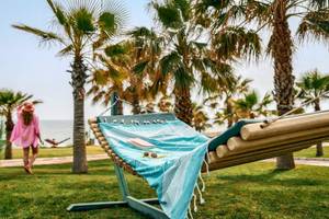 Ein Liegestuhl am Strand des Magic Life Jacaranda Hotels mit einer Person im Hintergrund, die einen Hut und eine Sonnenbrille trägt.