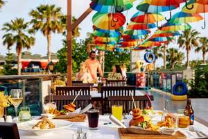 Terrasse im Magic Life Jacaranda Hotel mit bunten Regenschirmen, bunten Tischen und Stühlen, Essen und Getränken.