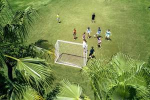 Kinder spielen Fußball auf einem grünen Rasenfeld im Magic Life Jacaranda Hotel.