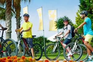 Drei Radfahrer im Magic Life Jacaranda, zwei in Helmen, einer mit Rucksack, auf gut gepflegtem Rasen.