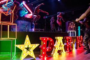 Party auf der Bühne im Magic Life Jacaranda Hotel mit leuchtenden Neon-Lettern und tanzenden Gästen.