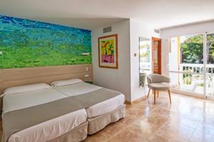 Doppelzimmer im Canyamel Classic Hotel mit zwei Betten, buntem Wandbild, und Zugang zu einer Terrasse.