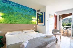 Hotelzimmer im Canyamel Classic mit Doppelbett, Kunstwerk an der Wand und Balkonzugang.