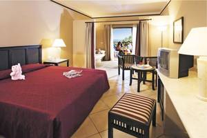 Innenansicht eines Hotelzimmers im Jaz Belvedere Resort mit einem Doppelbett, Möbeln und Aussicht auf den Balkon.