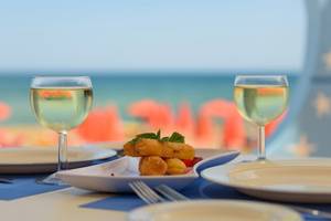 Zwei Gläser mit Wein und einem Teller mit frittierten Speisen auf einem Tisch mit Blick auf das Meer.
