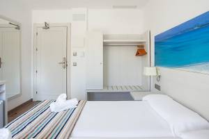 Rosales Formentera Hotelzimmer mit weißem Bett, Decken, Kissen und Badezimmerspiegel.
